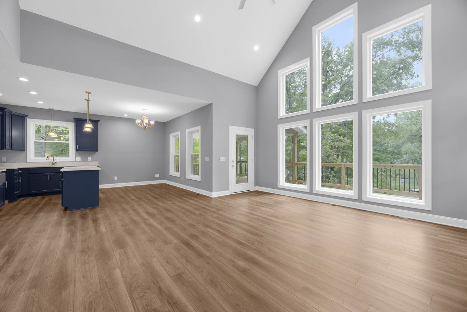 Spacious room with hardwood flooring, multiple large windows, blue cabinet with white countertop, white door with glass panel, and interior railing