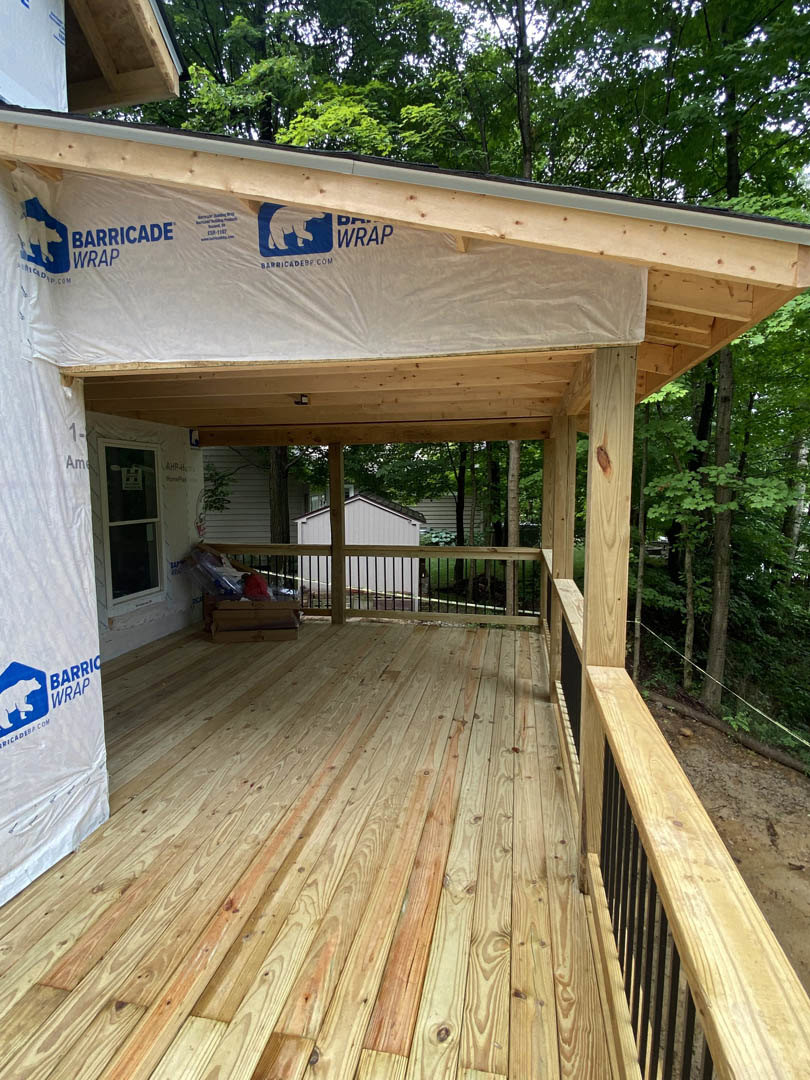 Wooden deck with railings and covered porch, plank ceiling, surrounded by trees; window features a sign with a white bear on a blue background.