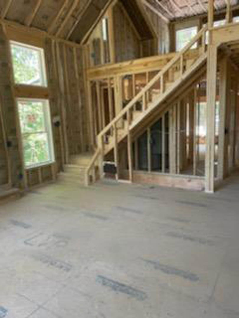 Wooden staircase with hardwood steps and railing, adjacent to a room featuring wooden plank flooring, white walls, and a window with natural light.