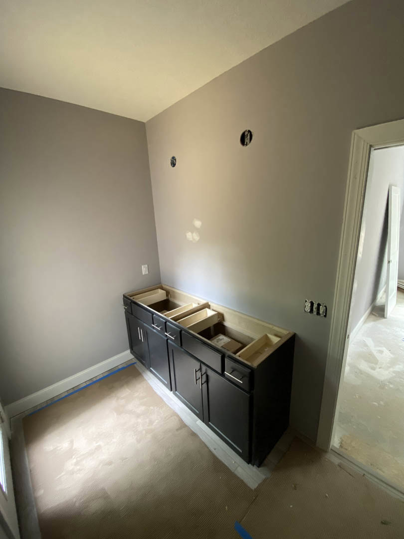 Black kitchen cabinets with drawers, white door, carpeted flooring, plaster walls, and natural light casting shadows in a modern kitchen