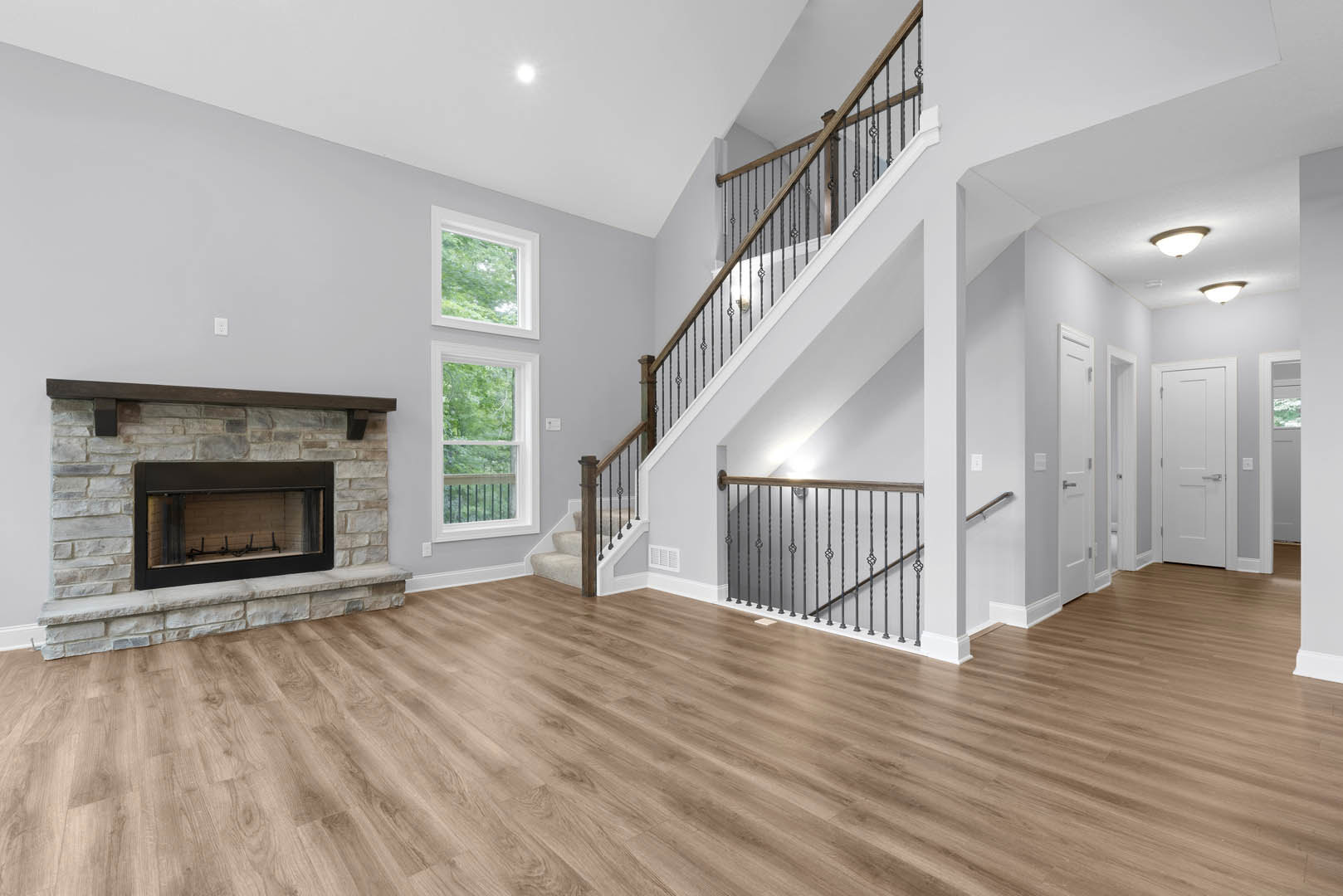 Living room with hardwood floors, white plaster walls, wood-framed fireplace containing metal accents, staircase with metal railing, and white door with silver handle