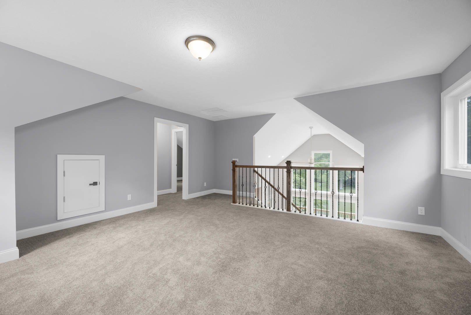 Carpeted floor with metal railing staircase, open white door, white walls, ceiling light fixture