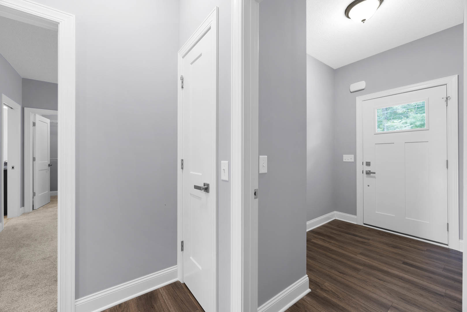 Hallway with white paneled doors, wood plank flooring, white walls, and a rectangular window with a white frame