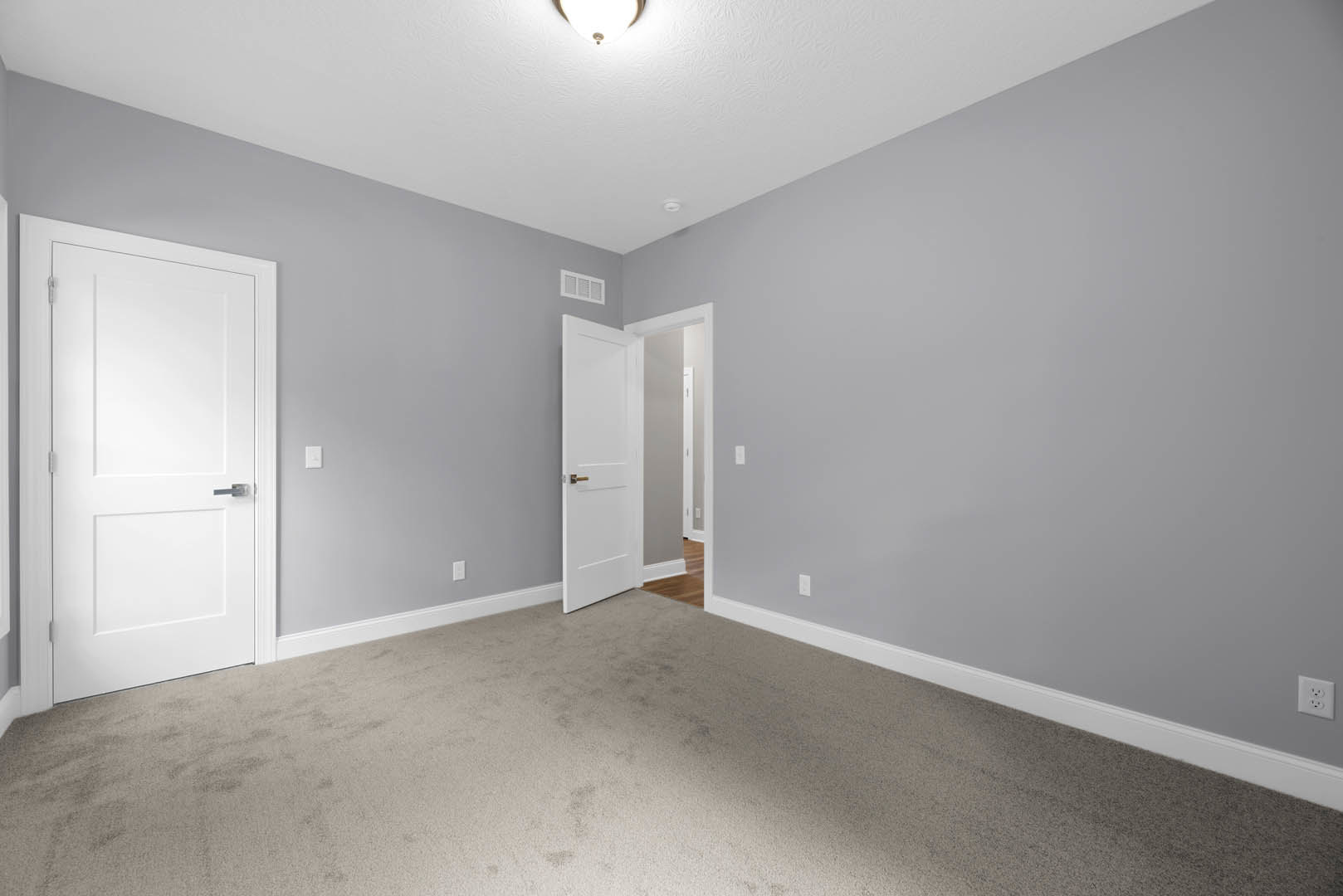 White paneled door with silver handle open to carpeted room, white walls, ceiling, and double electrical outlet visible