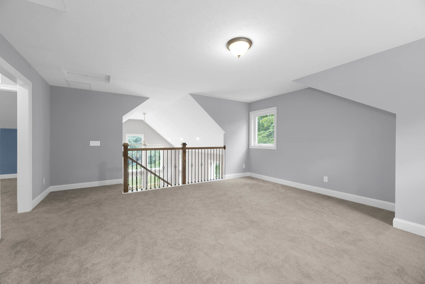 Carpeted room featuring a white-painted railing, large window overlooking trees, and recessed ceiling light fixture