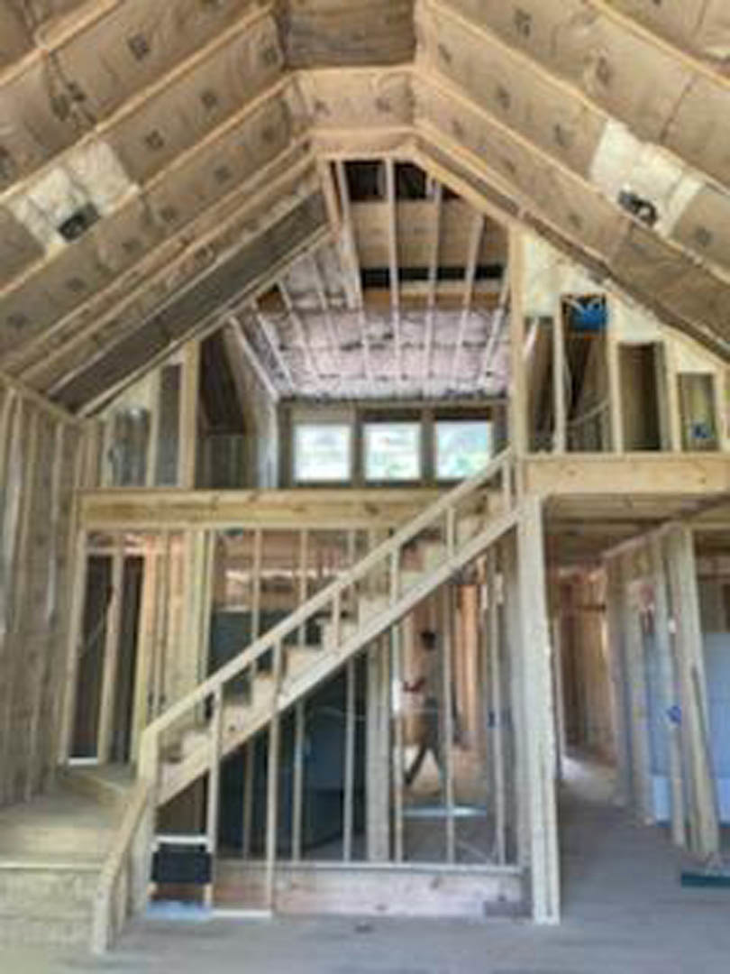 Wood-framed staircase in unfinished interior with exposed beams, plank flooring, and partially completed walls during home construction