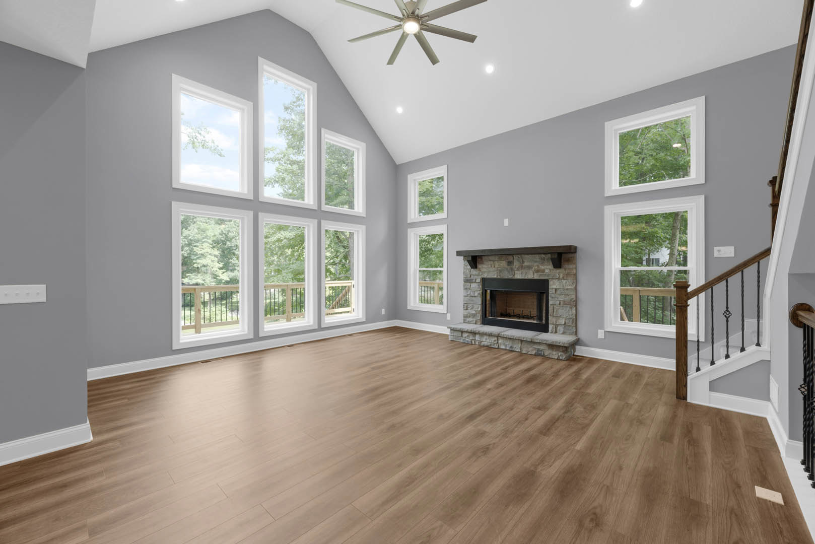 Hardwood floored living room with glass door fireplace, ceiling fan with light, and windows showing tree branches outside