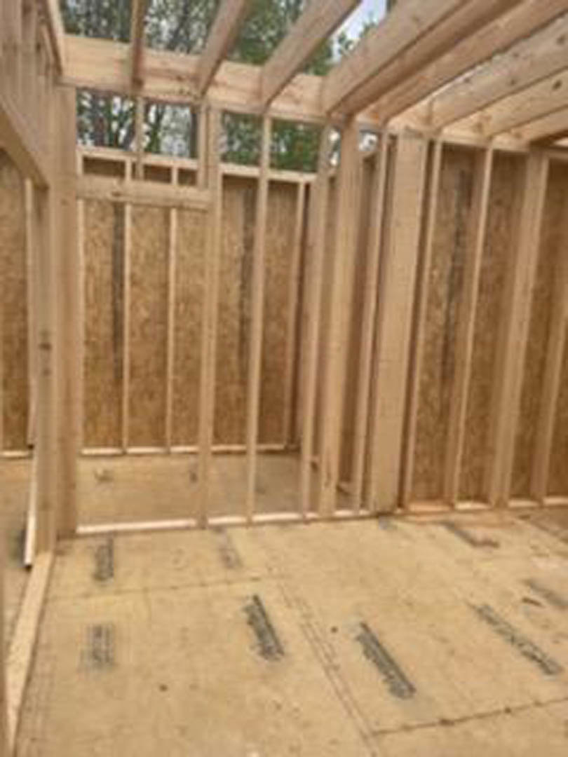 Unfinished room featuring exposed wood beams, plywood subfloor, and framed walls with visible lumber