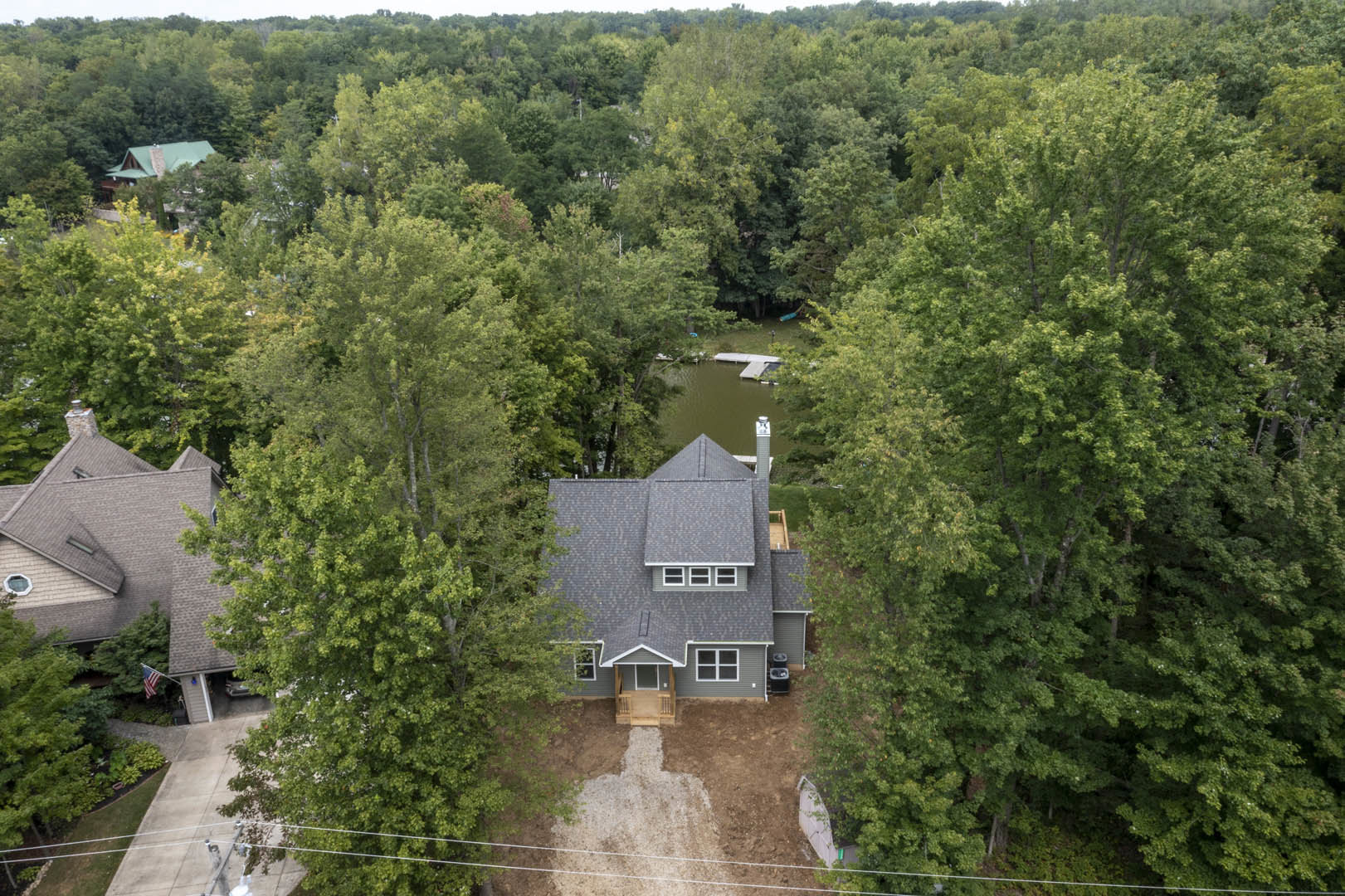 Modern two-story home with gray siding and large windows, nestled among mature trees with lush greenery and blue sky in the background