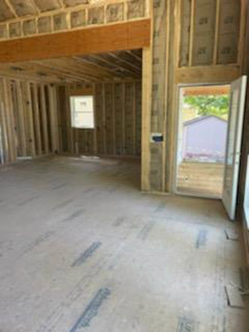Open doorway leading into a room with light wood plank flooring, white walls, and natural light filtering through a window