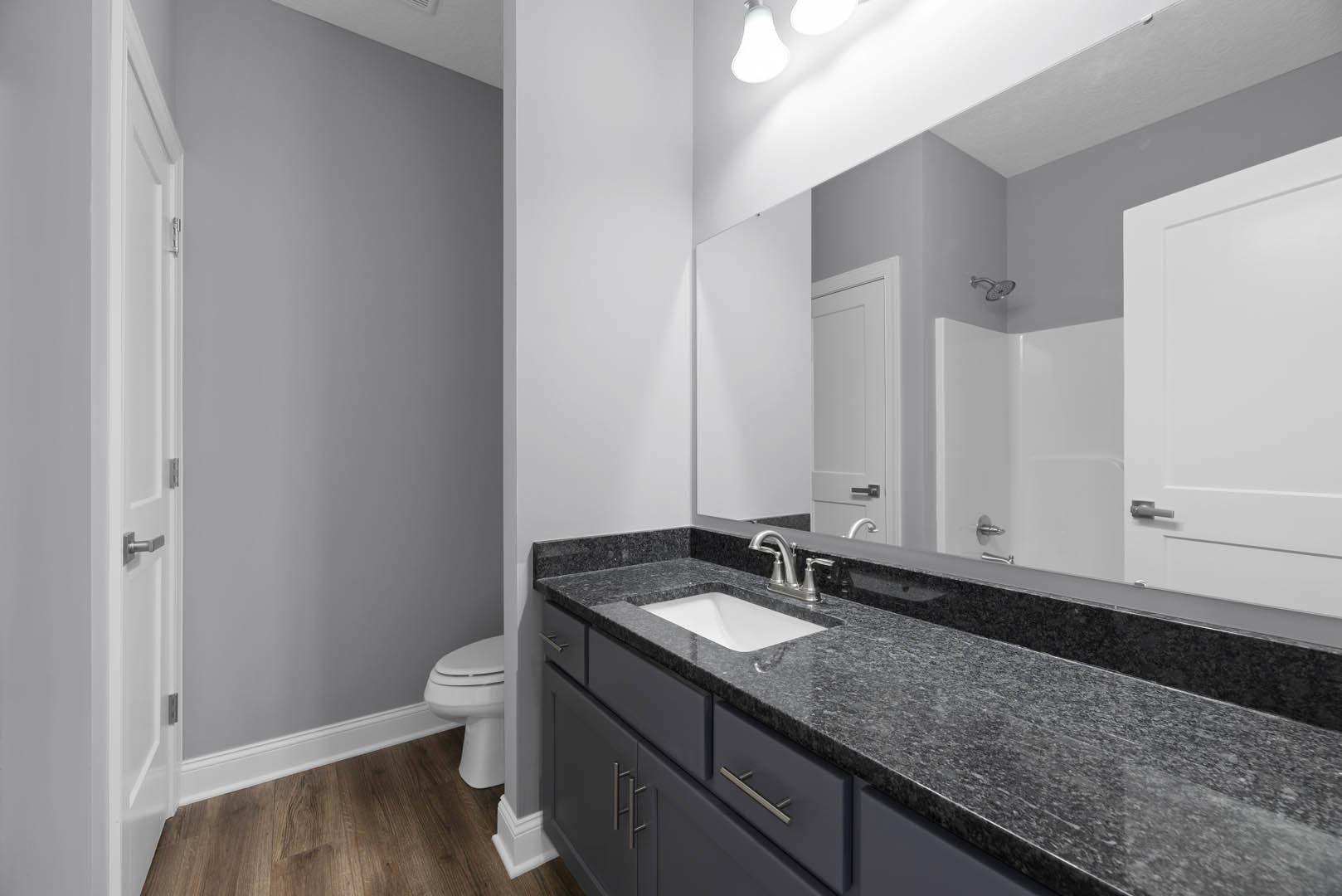 White sink with black countertop beneath a rectangular mirror, tile backsplash, modern faucet, and partial view of toilet in a contemporary bathroom.