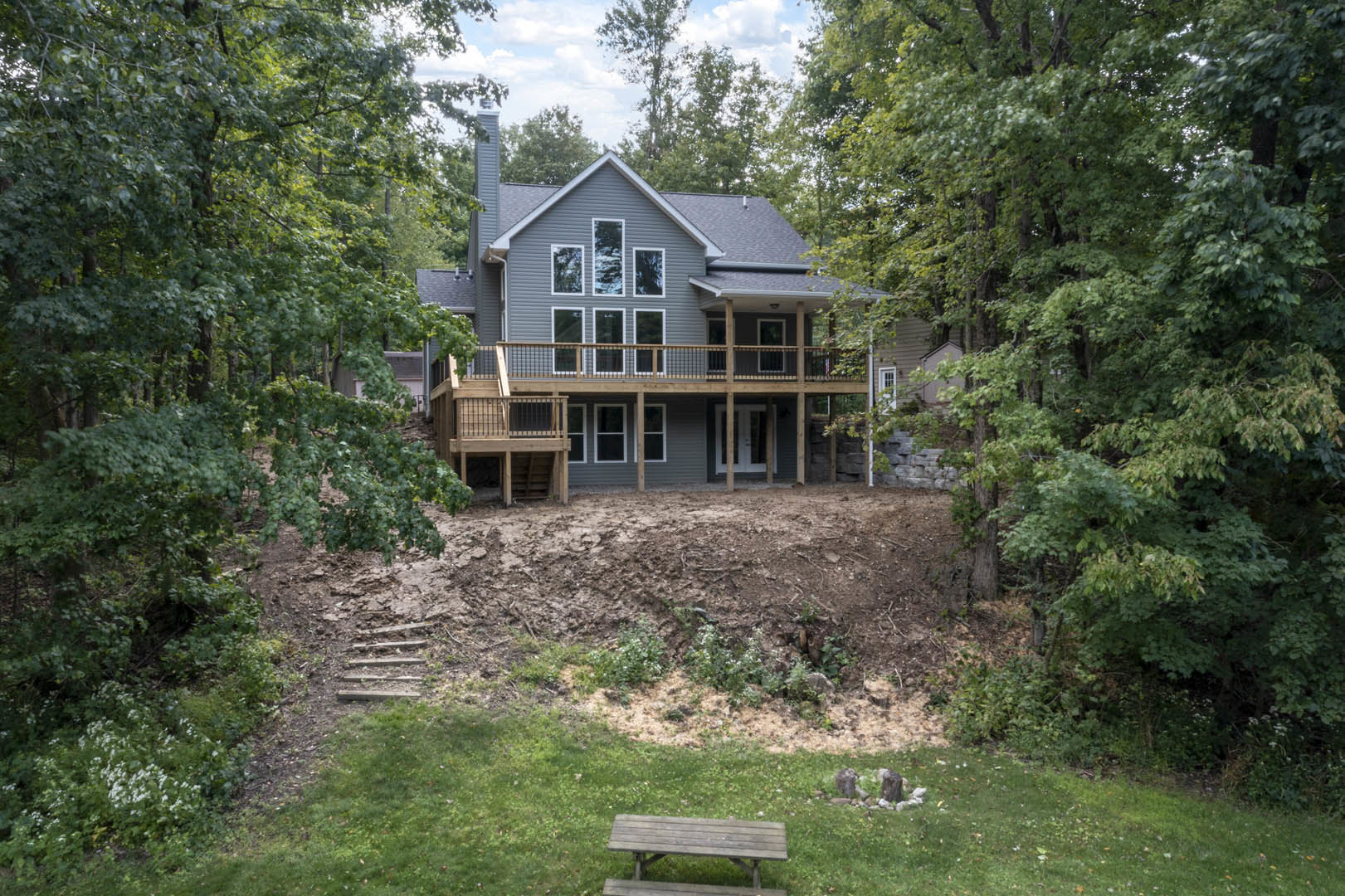 Backyard deck with wooden picnic table, grassy lawn, tree stump, and cottage-style house exterior