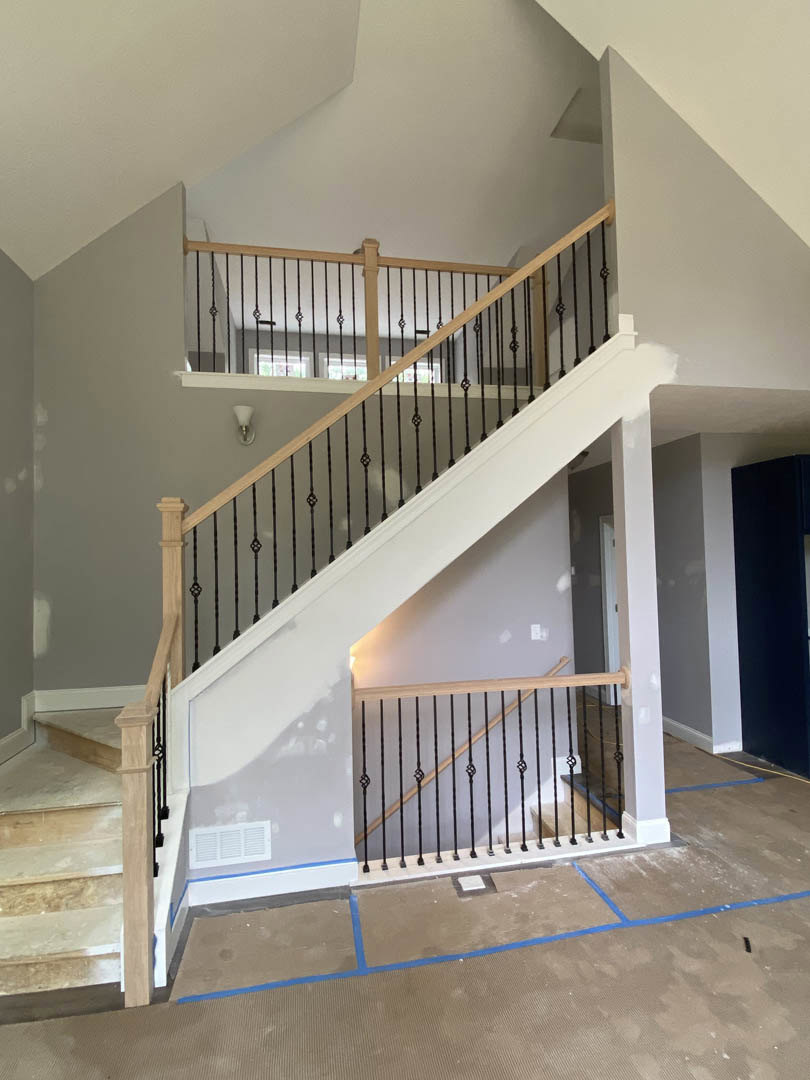 Modern staircase with metal railings, black accent wall with white border, white plaster walls, and hardwood flooring