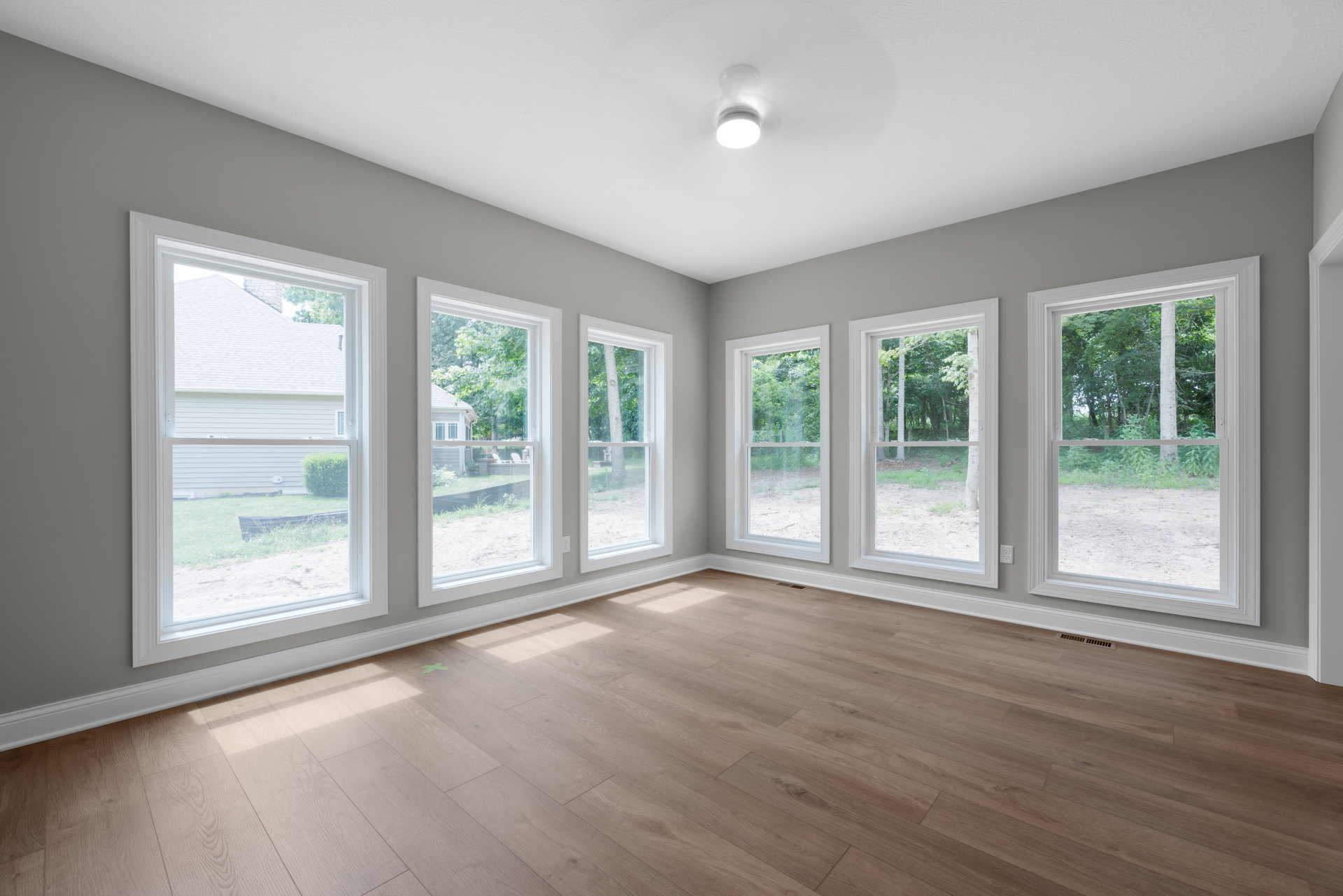 Spacious room with wood flooring, multiple large windows, and views of greenery outside