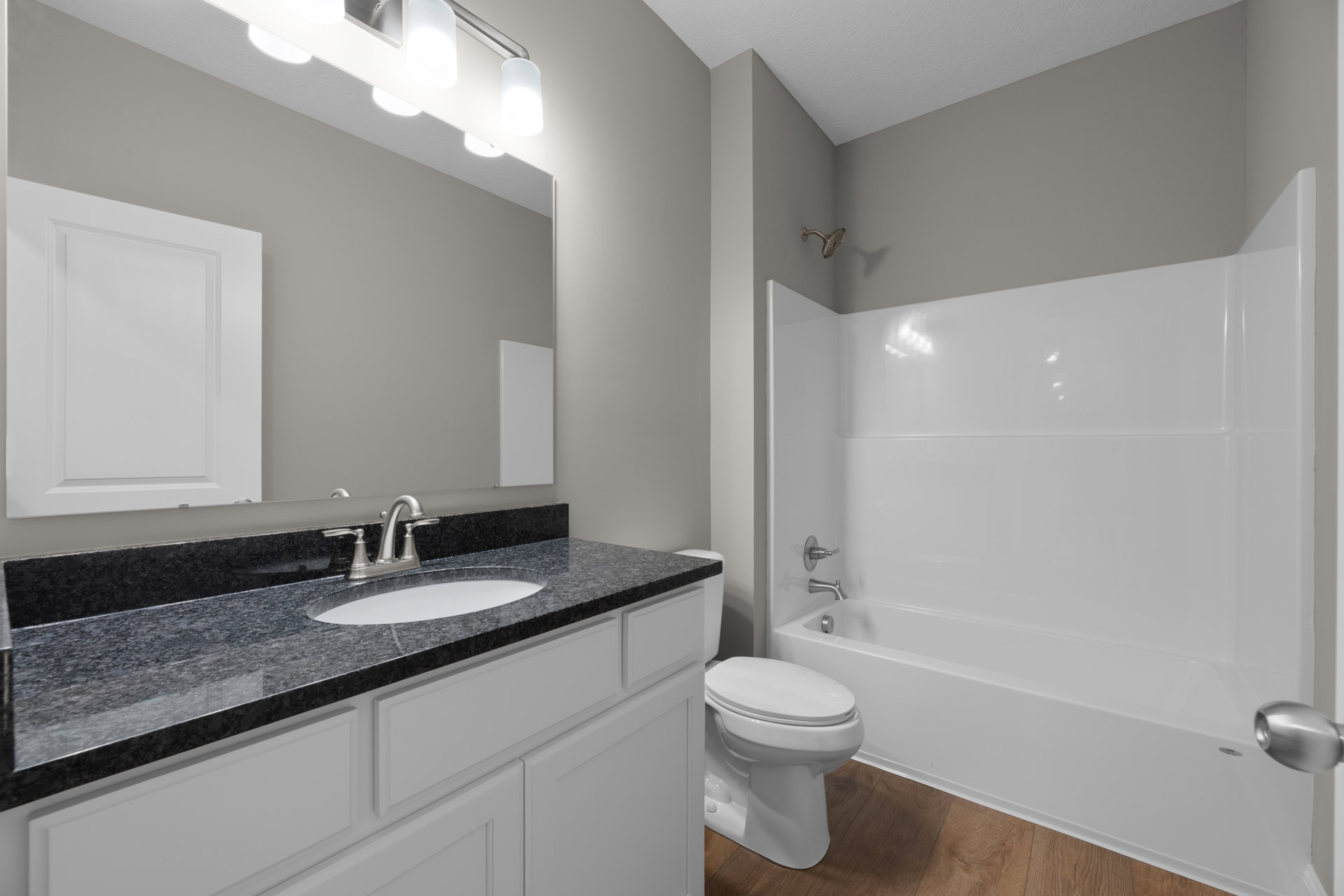 Bathroom with white bathtub, white toilet, and sink on tiled floor; chrome faucet and knob; white door with matching frame; neutral wall tiles and countertop.
