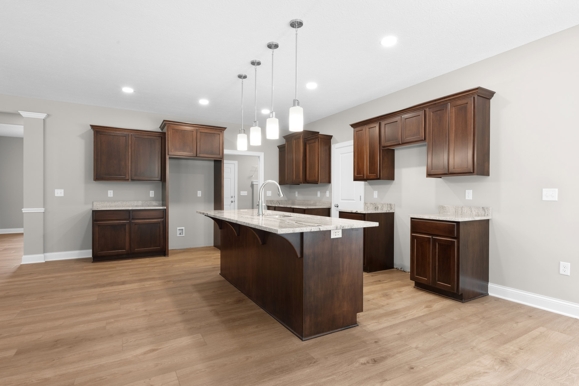 Dark wood kitchen cabinets with white marble countertops, central island featuring an undermount sink, stainless steel appliances, and hardwood flooring