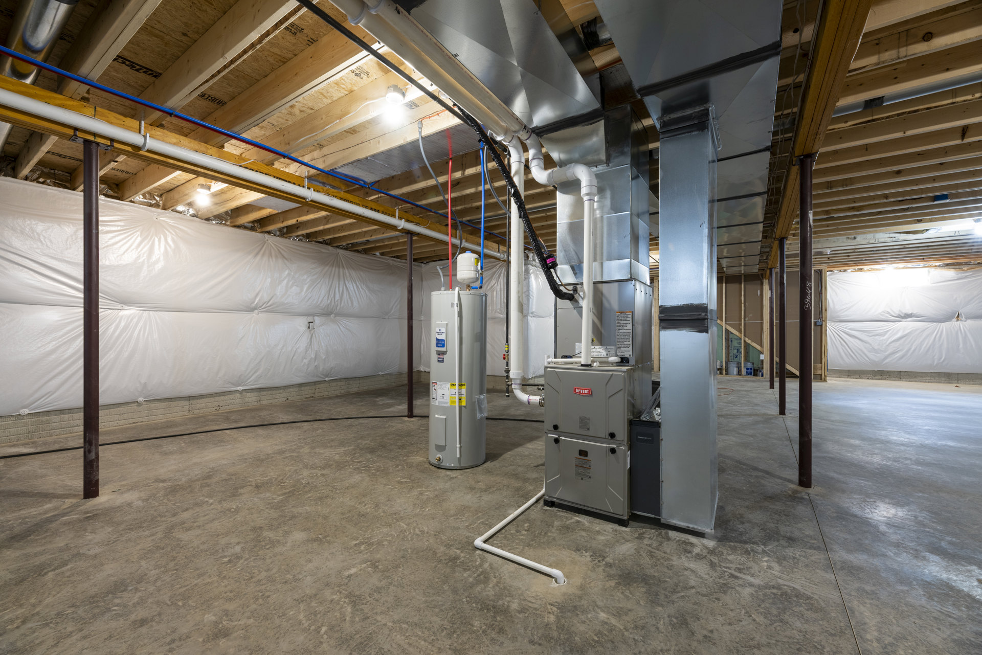 Basement utility room with exposed steel and aluminum pipes, white cylindrical tank with blue label, white and black walls, white plastic sheeting covering part of the wall