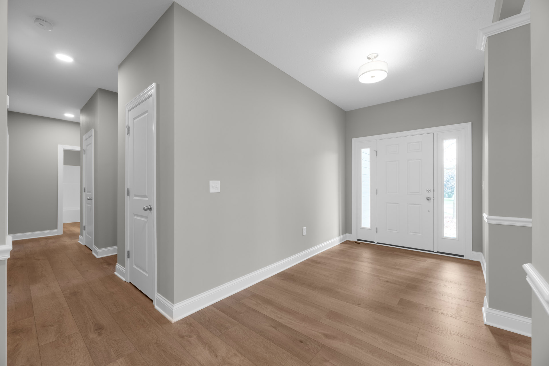 Hallway with white paneled doors, wood flooring, white baseboards, and a white ceiling light fixture