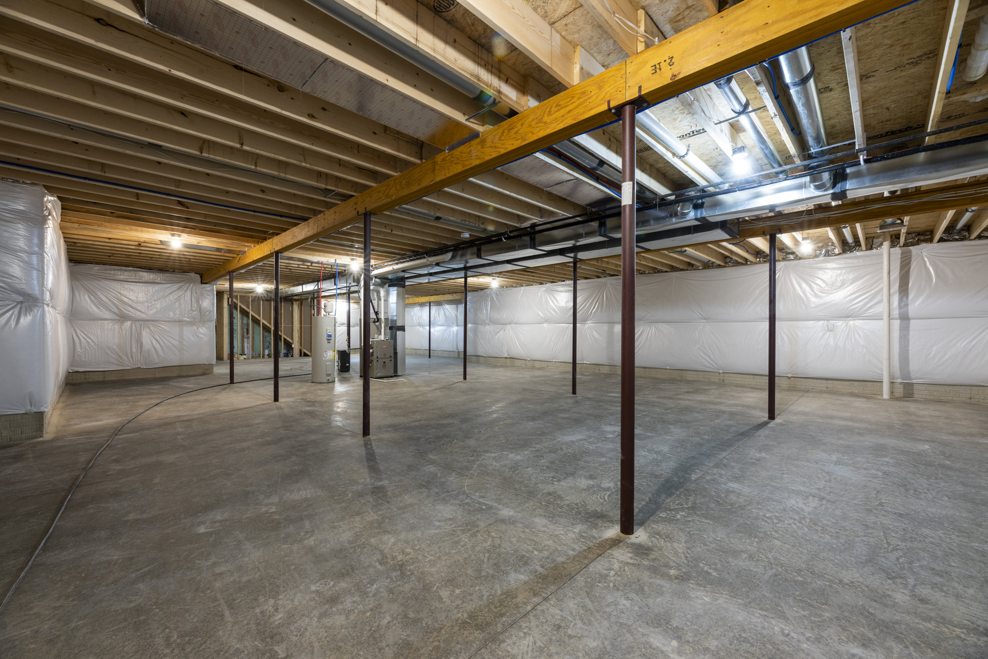 Concrete floor and white wall with exposed wooden ceiling beam and metal support poles, basement interior with white plastic wall covering.