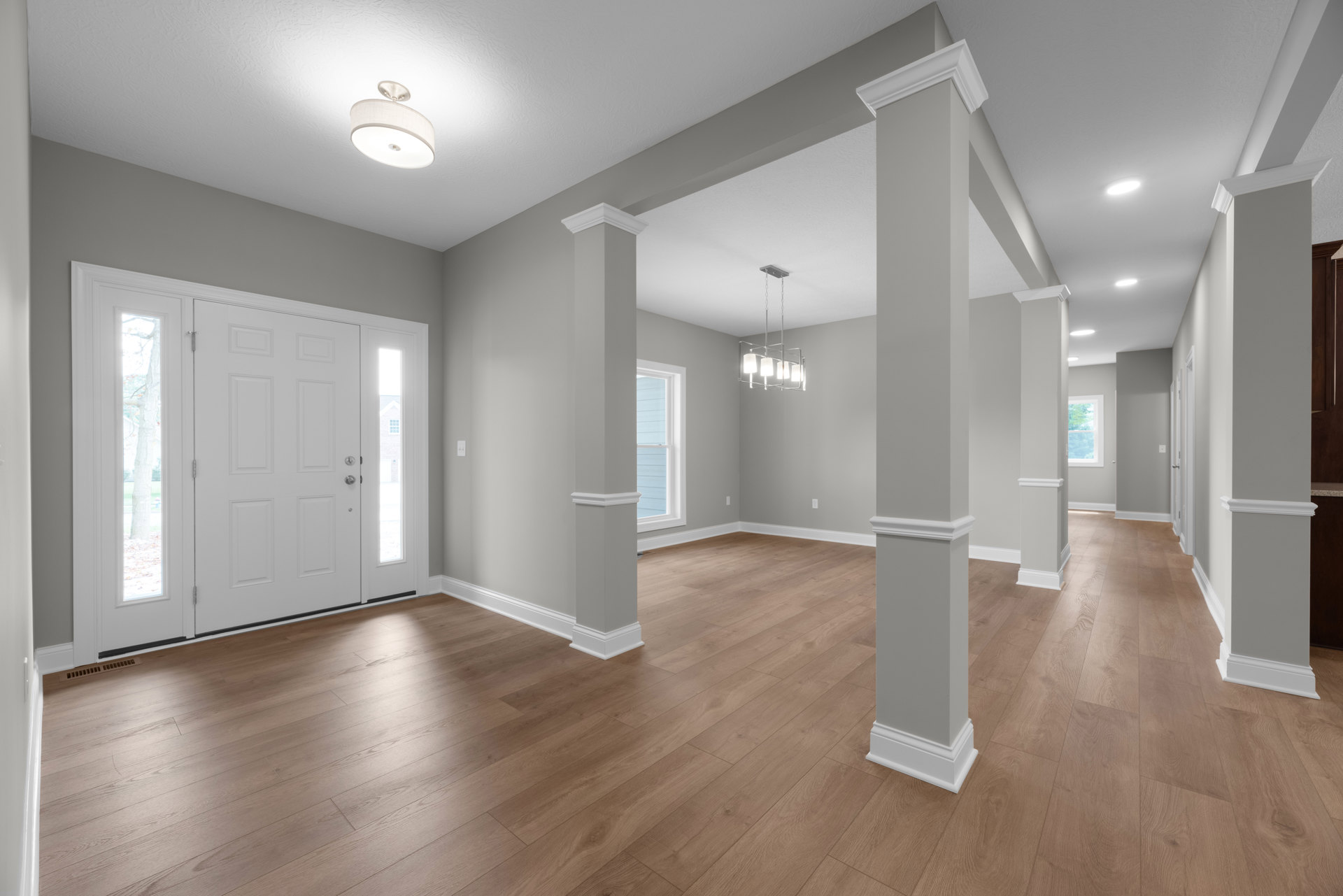 White columns frame a spacious room with hardwood floors, blue accent wall, ceiling light fixture with white shade, large window, and white door with glass panels.