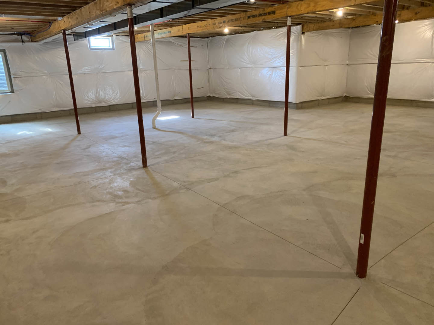 Concrete floor with white walls, exposed wooden ceiling beam, white pipe along wall, and white plastic coverings in a modern interior room