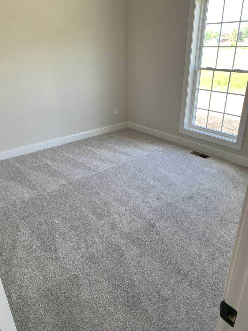 Carpeted room with white walls, large window overlooking green lawn, natural light illuminating neutral finishes