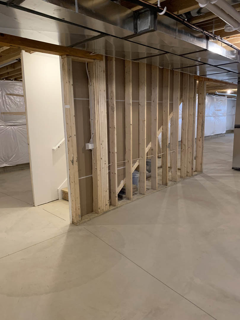 Room with exposed metal ceiling, plaster walls, concrete floor, whiteboard with handle mounted on wall, plastic wrap covering section of wall, visible door.