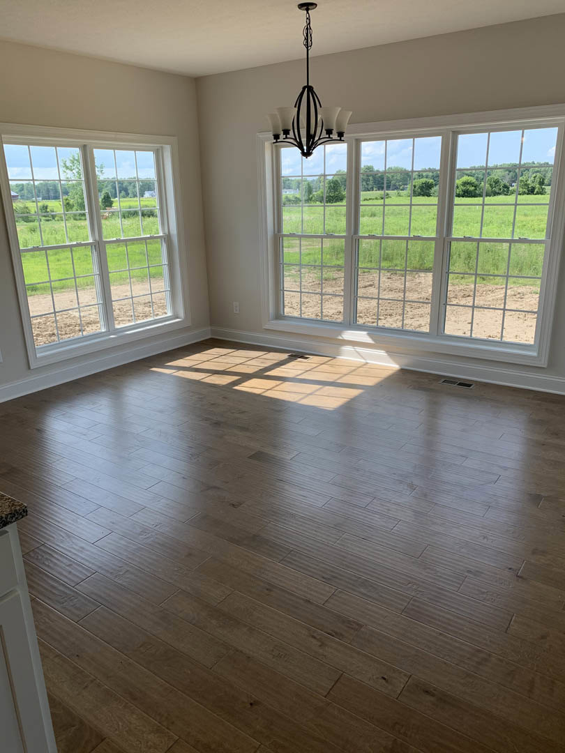 Spacious room featuring wide plank wood flooring, expansive multi-pane windows, white walls, and natural daylight illuminating the interior