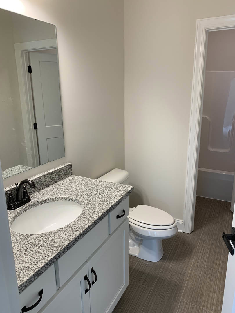 Modern bathroom with white ceramic sink, chrome faucet, and matching toilet; light-colored tile walls, white door with silver handle, and minimalistic cabinetry.