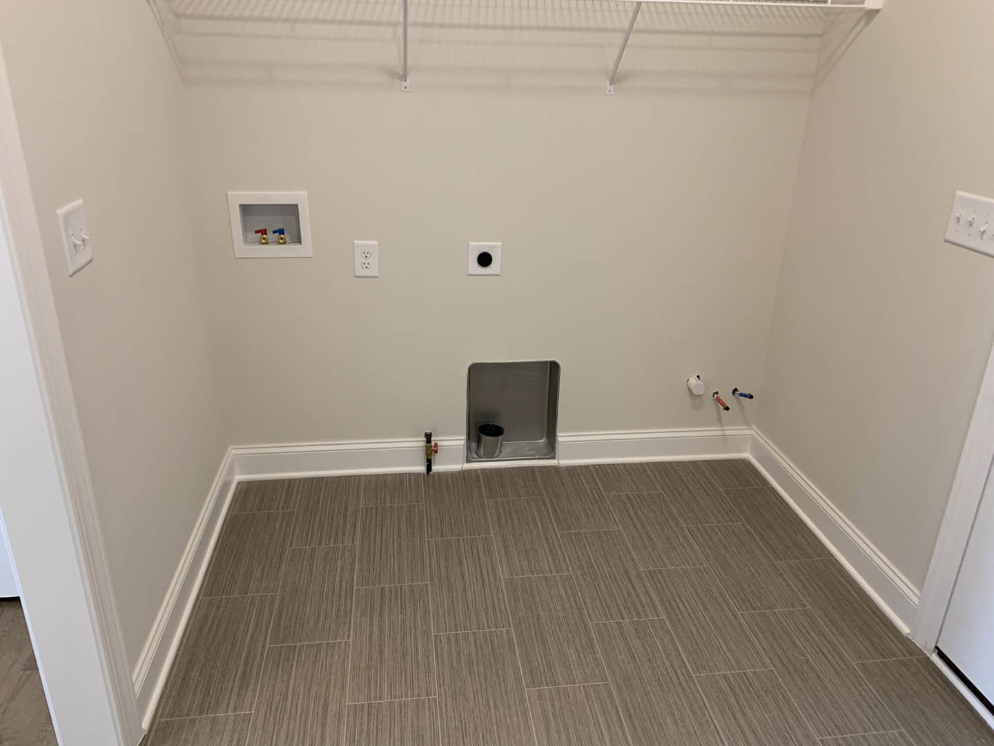 Bathroom with light wood flooring, white plaster walls, and a metal box fixture near the floor.