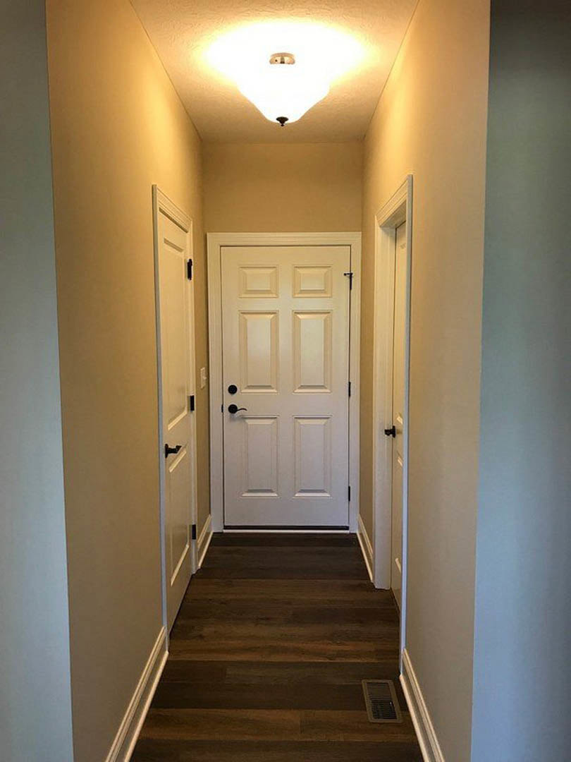 Hallway with dark wood flooring, white paneled doors, ceiling-mounted light fixture, and wall vent