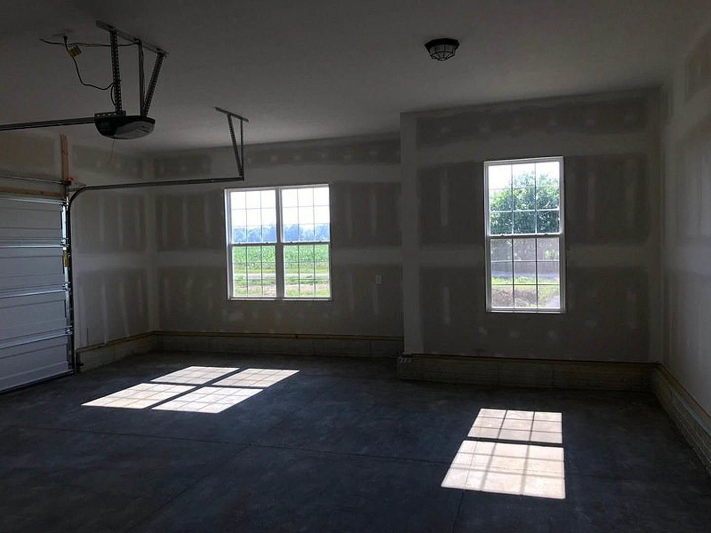 Spacious room featuring large windows overlooking a field and trees, ceiling fan, dark flooring with white square tiles, and light grey walls.