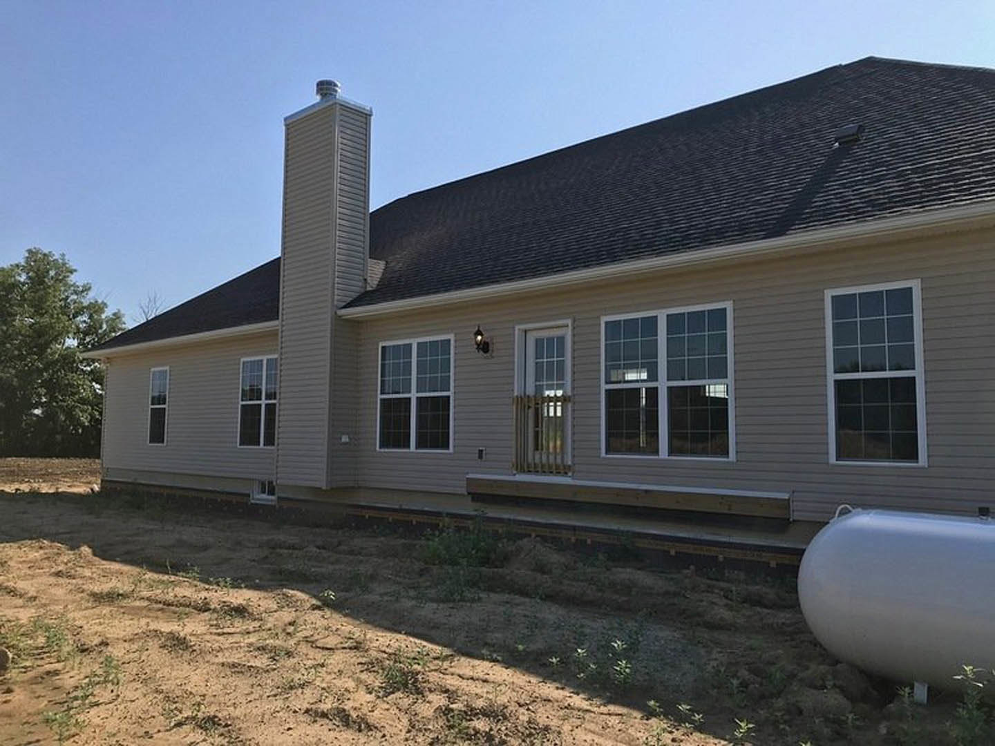 Two-story house with white siding, white-framed windows, brick chimney, and a large spherical white tank with a cord in the front yard; mature tree and blue sky in background