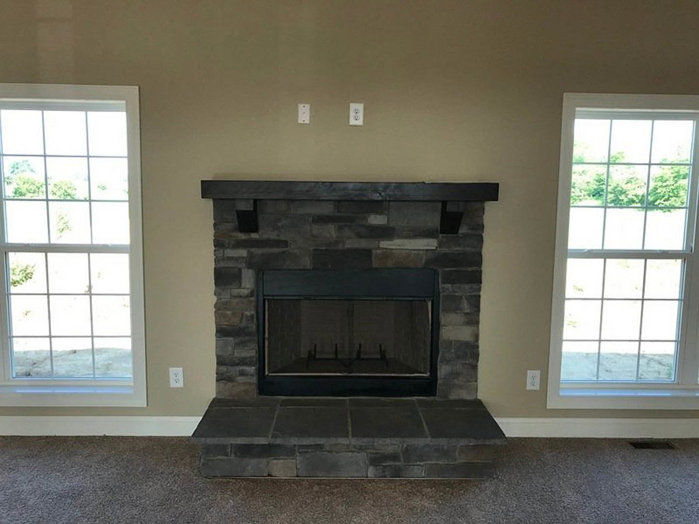 Stone fireplace with metal frame and hearth, surrounded by multi-pane windows, wood flooring, and textured stone wall.