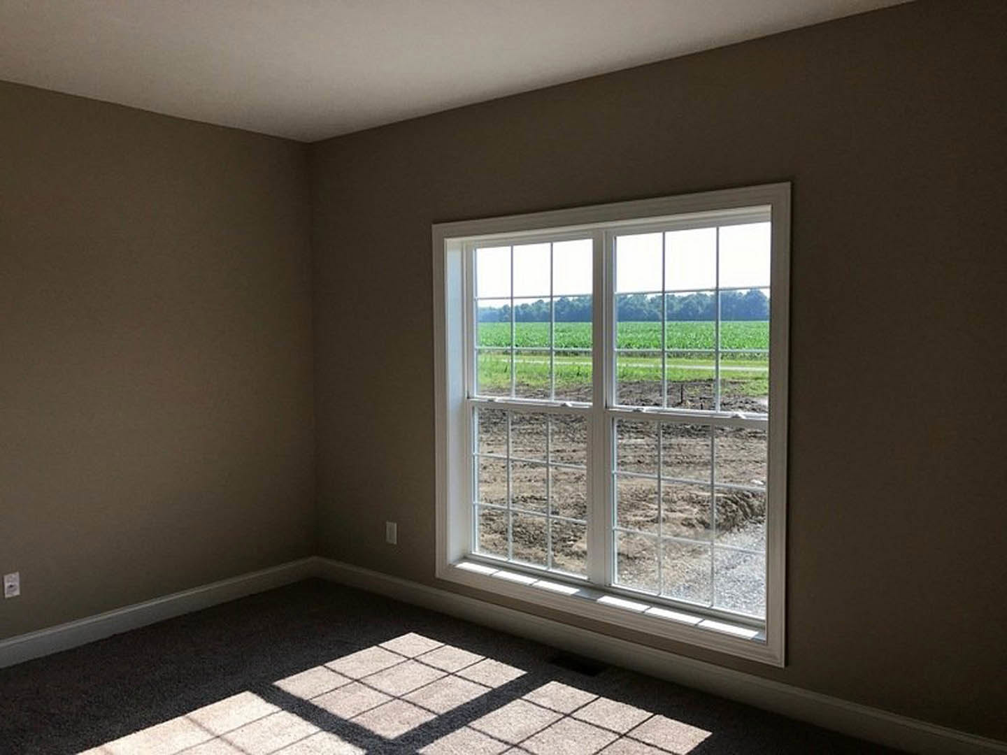 Sunlit room with tile flooring, large window, and views of grassy field and farmland outside