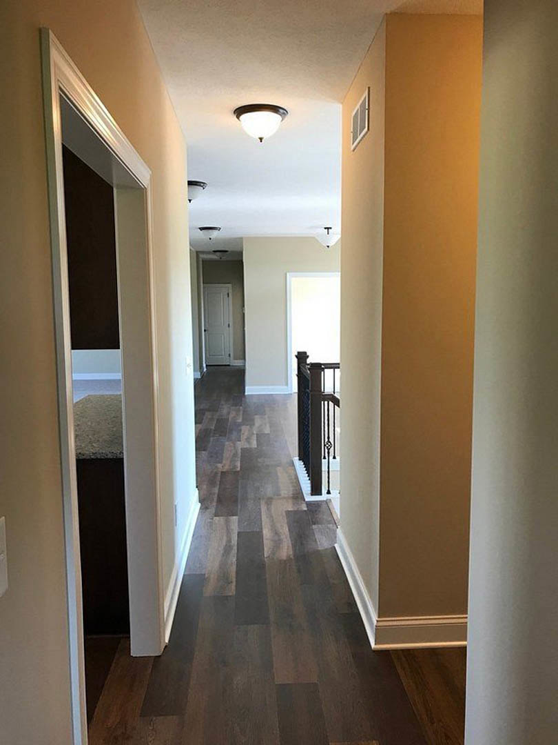 Hallway with warm wood flooring, white walls, black hardware on doors, round ceiling light fixture, and metal railing detail