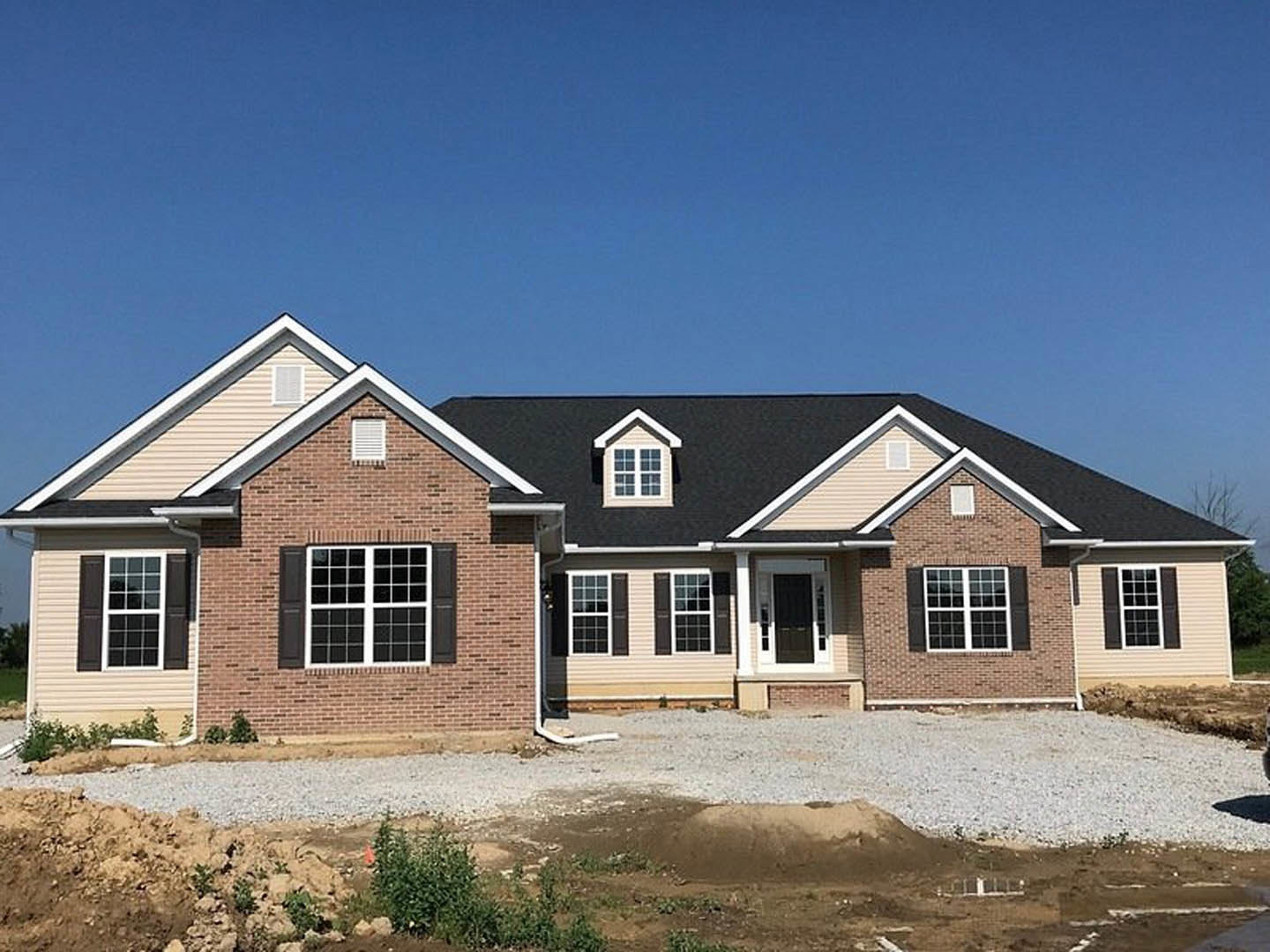 Modern custom home under construction with black roof, white-framed windows, white vent, close-up of entry door, gravel covering the ground, light-colored siding, and open sky
