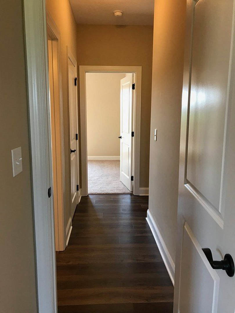 Hallway with dark wood flooring, white walls, and a white door featuring a black handle