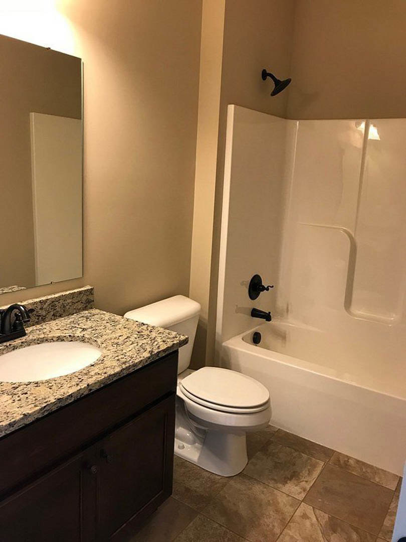 Modern bathroom with white tile walls, black faucet on rectangular sink, white toilet with closed lid, and partial view of bathtub