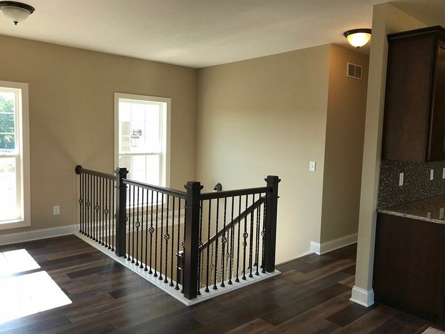 Wooden staircase with black metal railing, sunlight streaming through large window onto laminate flooring, modern ceiling light fixture above.