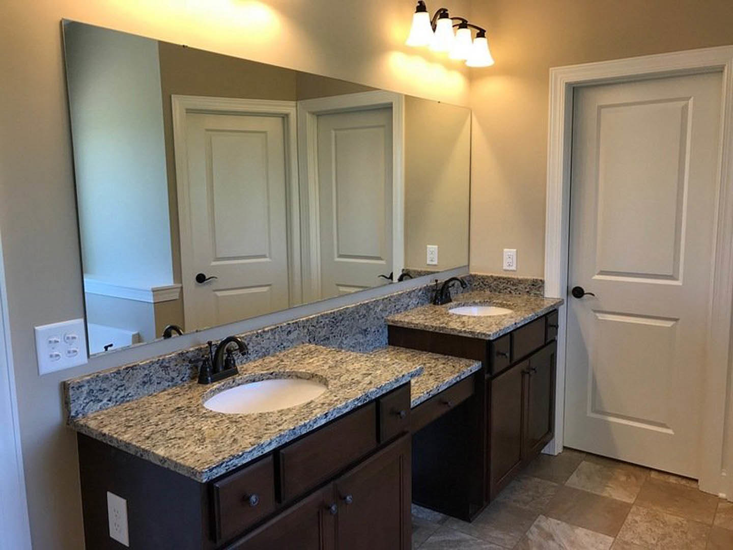 Bathroom with double sinks, white countertop, large frameless mirror, modern faucets, light fixture above, white cabinetry, black hardware, and tiled backsplash