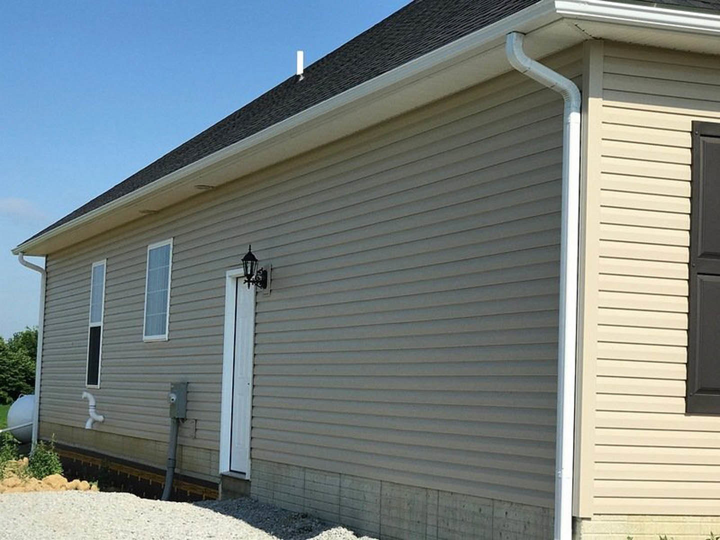 White front door with black trim, adjacent windows, light gray siding, covered porch, and gabled roof under blue sky