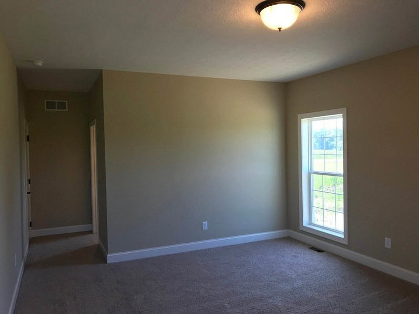 Carpeted bedroom with white walls, large window overlooking grassy yard, round ceiling light fixture, and simple trim detailing