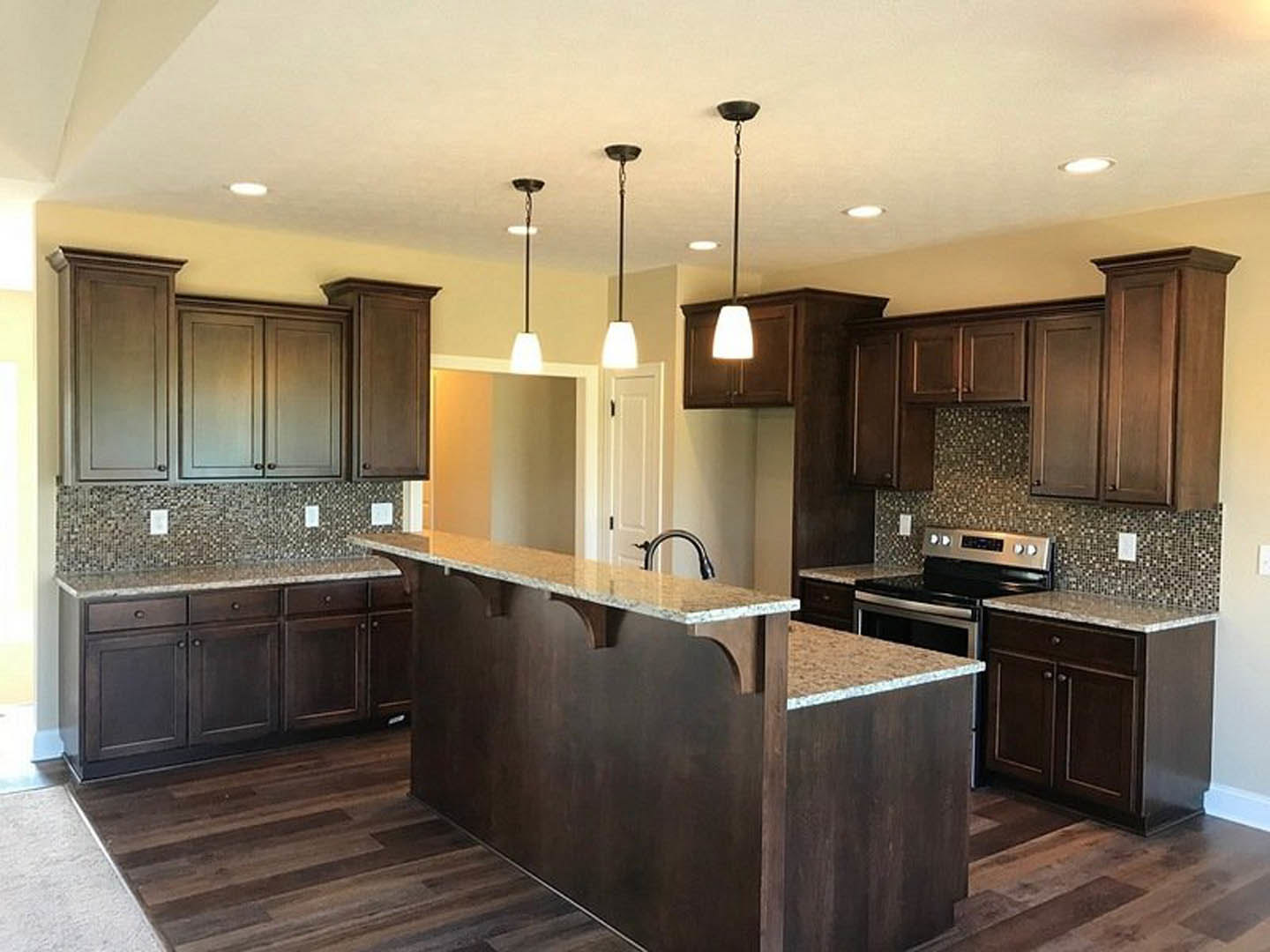 Open-concept kitchen featuring a tile backsplash, quartz countertop with built-in stainless steel stove, undermount sink, wood cabinetry, and pendant lights above a bar seating