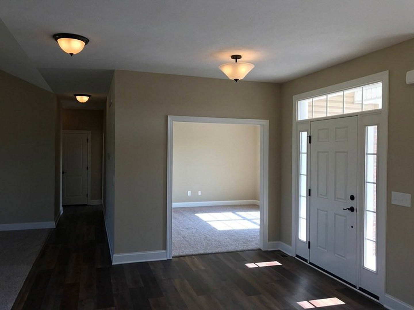 Hallway with white paneled doors featuring black handles, wood plank flooring, white walls, ceiling molding, and a modern light fixture