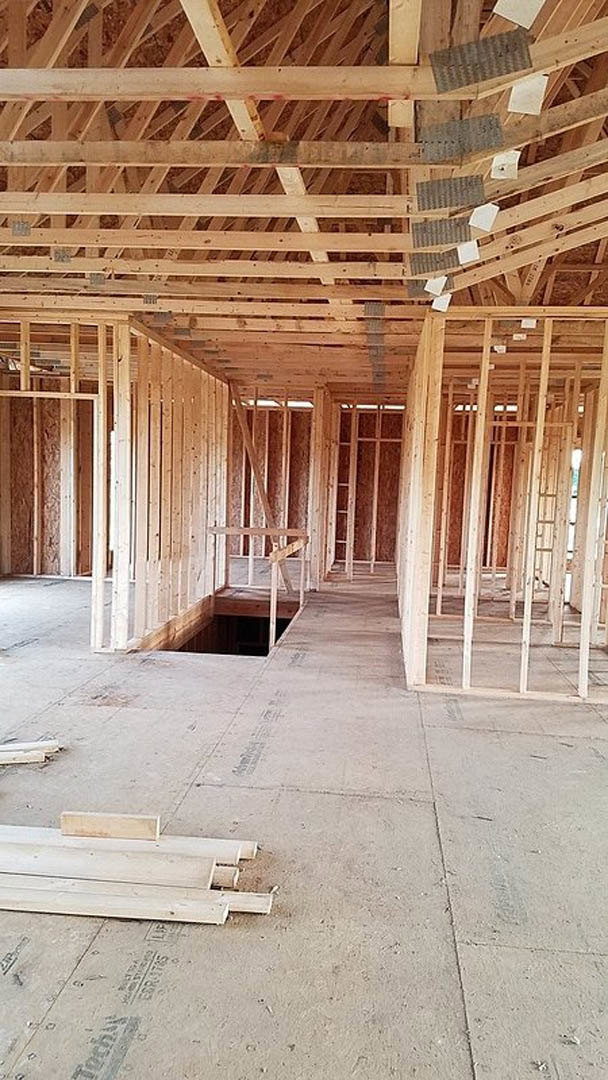 Exposed wood beams and planks on the floor in an unfinished interior, ceiling opening visible, construction materials and insulation present