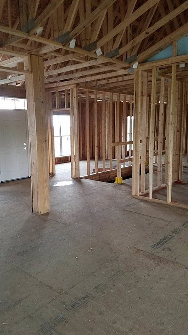 Wood-framed interior under construction with exposed beams, concrete floor, white door with knobs, and visible insulation materials