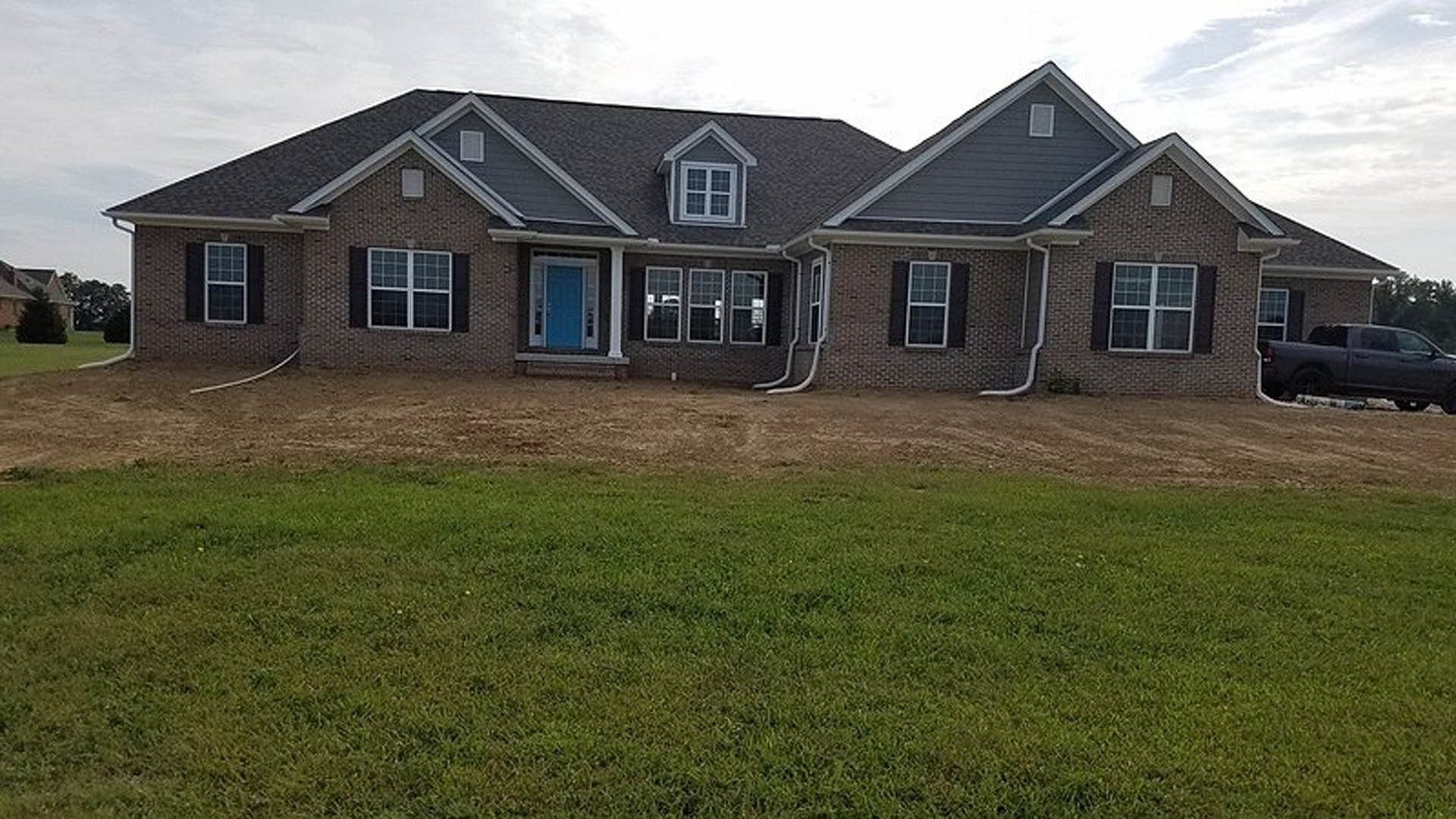 Two-story home with light siding, large windows, and gabled roof, surrounded by green lawn; black pickup truck parked on driveway.