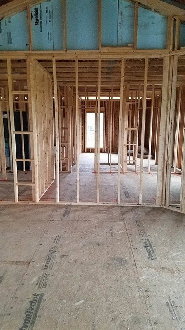 Living room featuring a wall clad in vertical wood planks, light-colored flooring, large window with black trim, and a modern concrete accent surface