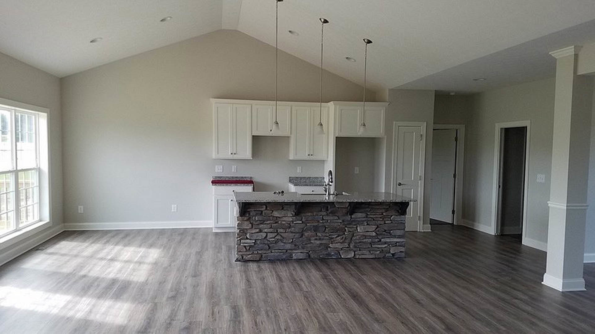 Open kitchen featuring a stone island with white cabinetry and red countertop, stone fireplace with matching countertop, tile flooring, plaster walls, and blurred figure in